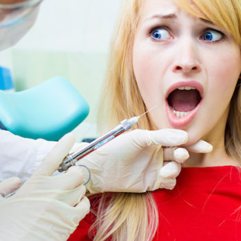 Closeup portrait terrified girl woman scared of needles, syringes, dentist visit siting in chair, opened mouth doesn't want dental procedure drilling tooth extraction isolated clinic office background