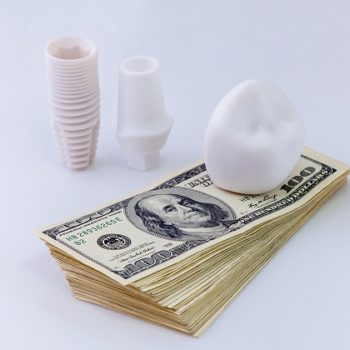 Dental implant on money.The dental implant construction is laying on the pack of dollars on white background.