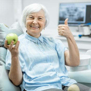 Portrait of a beautiful senior woman with healthy smile holding green apple at the dental office